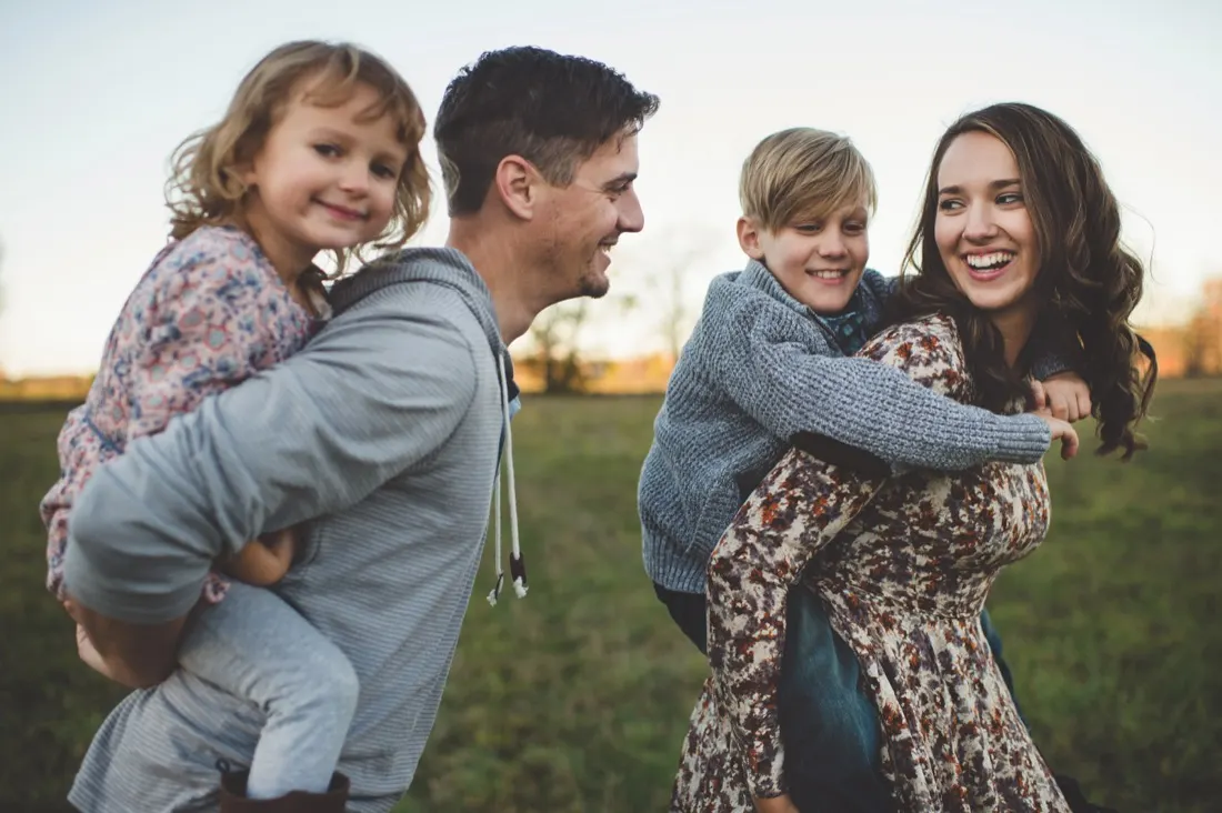 Two parents carrying their children piggyback in a field