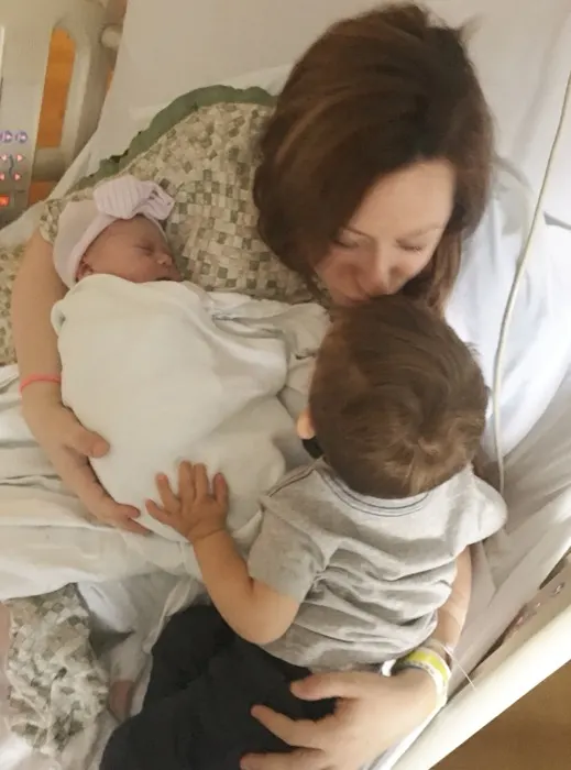 A mother holding her newborn while a toddler leans in